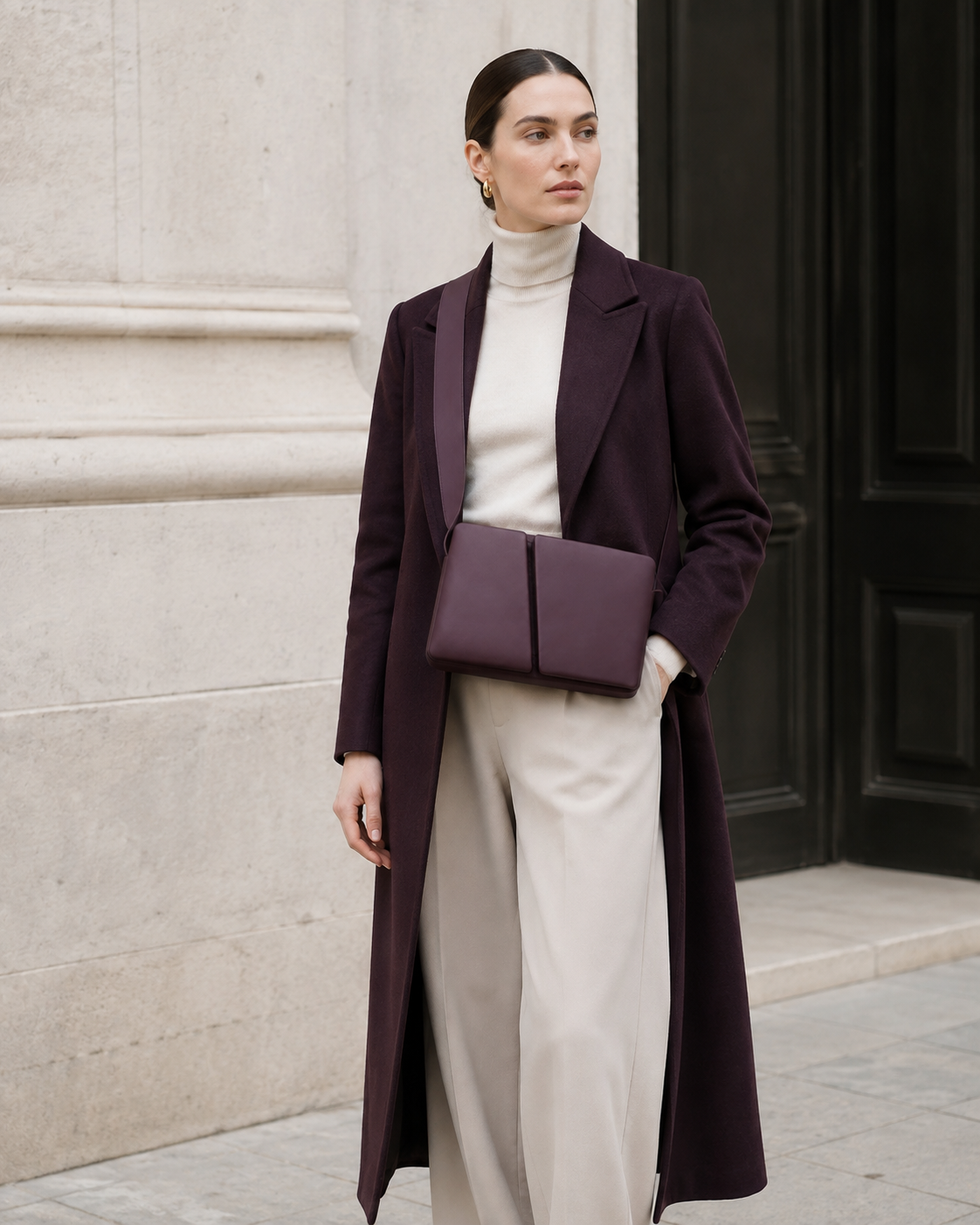 Woman in tailored neutrals carries the deep plum MUYLOTTA ML-CB04 crossbody bag by a limestone wall.