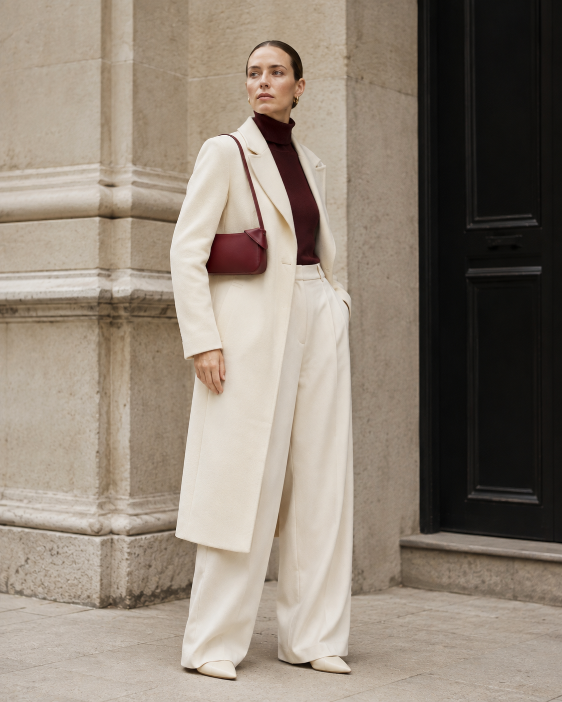 Woman in tailored neutrals carries the burgundy MUYLOTTA ML-SH05 shoulder bag on her shoulder by a limestone wall.